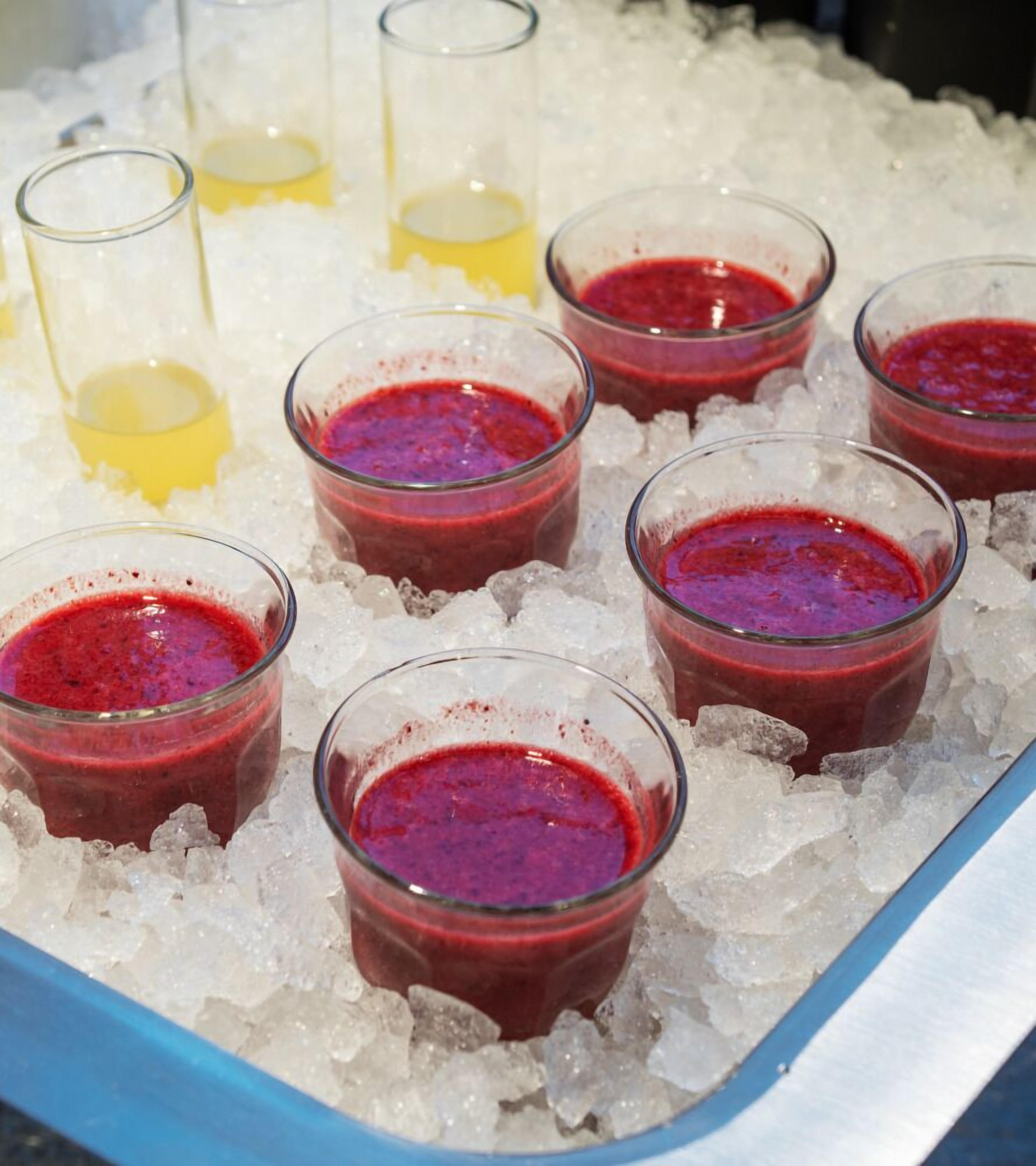 A tray of glasses filled with red beverages, possibly cocktails, on a bed of ice.
