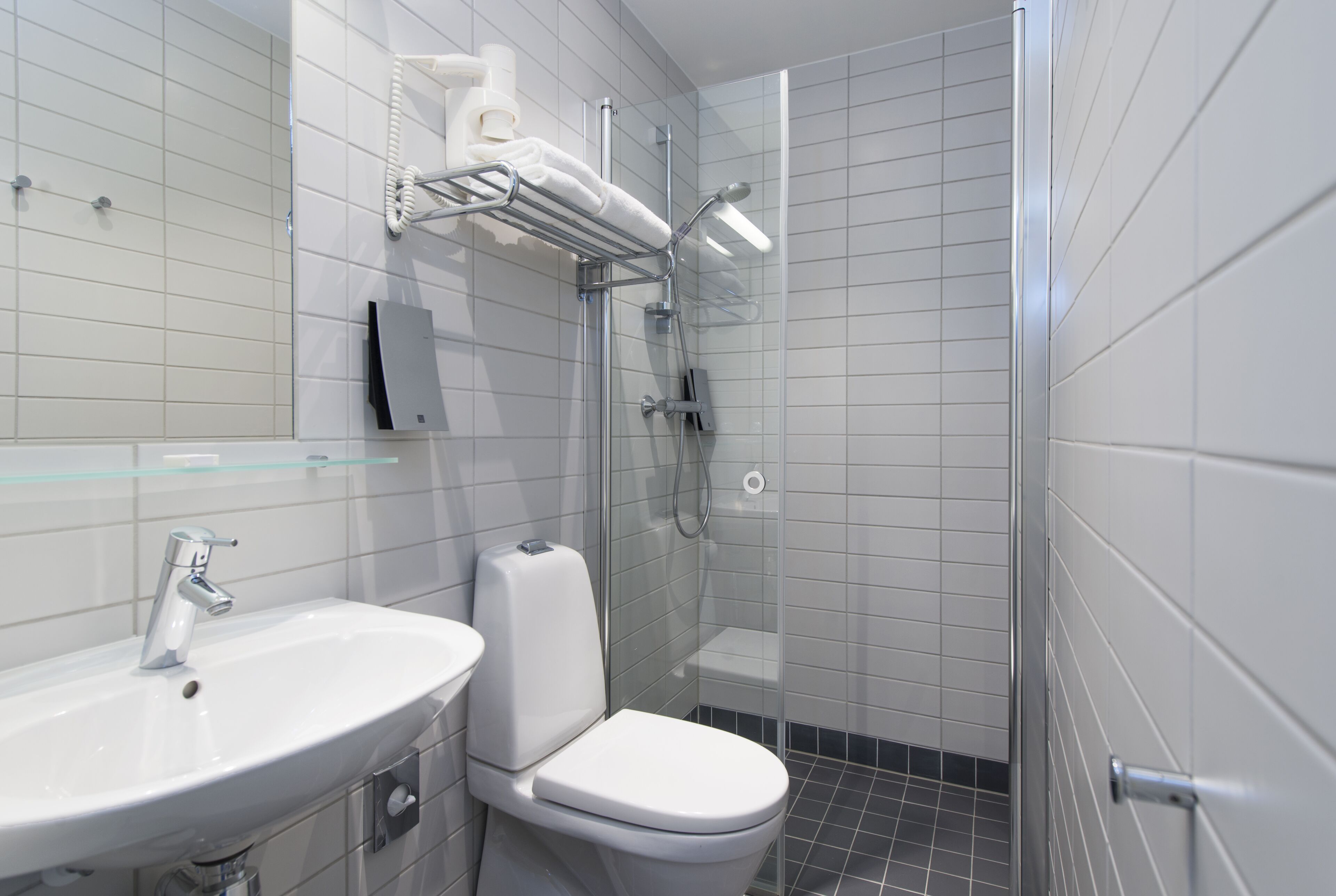 Et moderne badeværelse med hvid vask, toilet og brusekabine i glas.