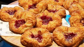 Una presentación de pasteles, incluyendo croissants con mermelada, sobre una tabla de madera.