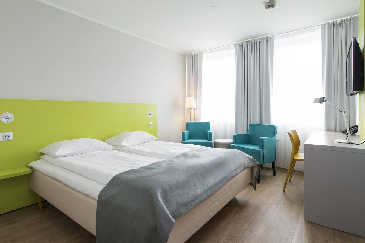 A hotel room with a bed, two chairs, a desk, and a TV.
