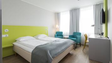 Una habitación de hotel con cama, dos sillas, un escritorio y televisión.