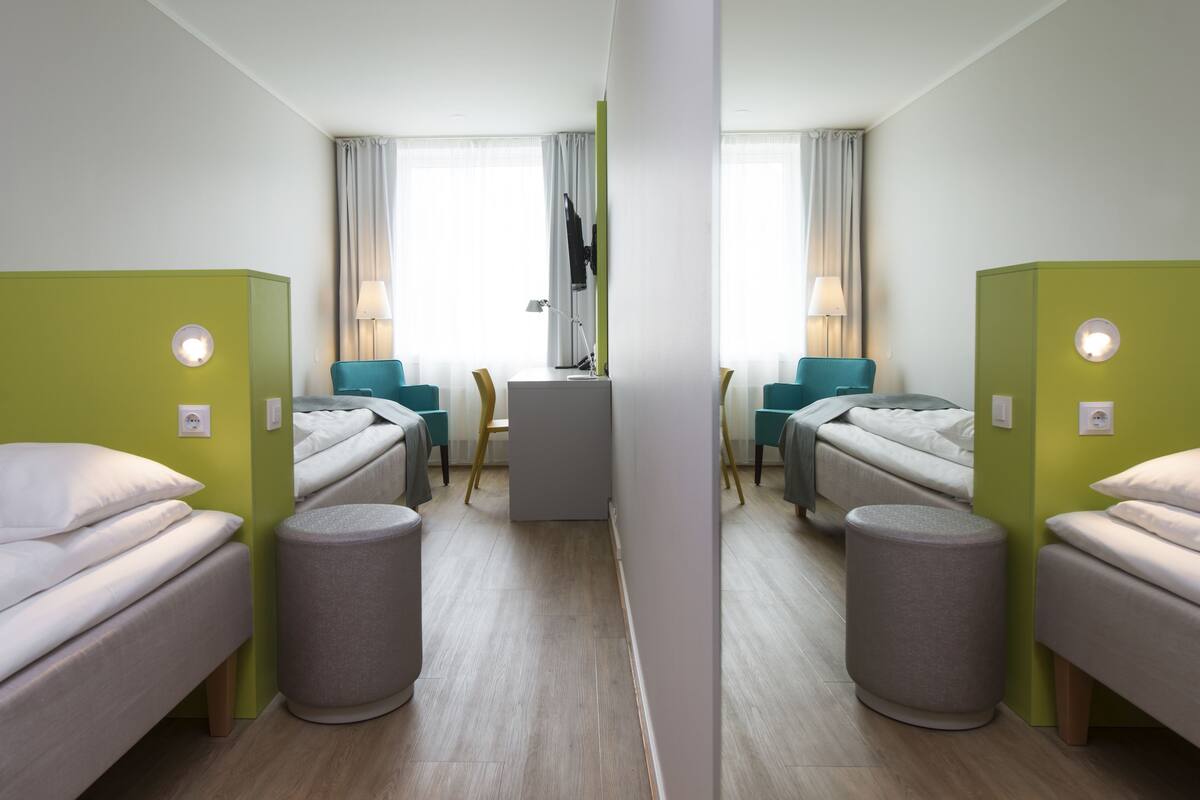 A hotel room with two beds, a desk, two chairs, a mirror, and a TV.