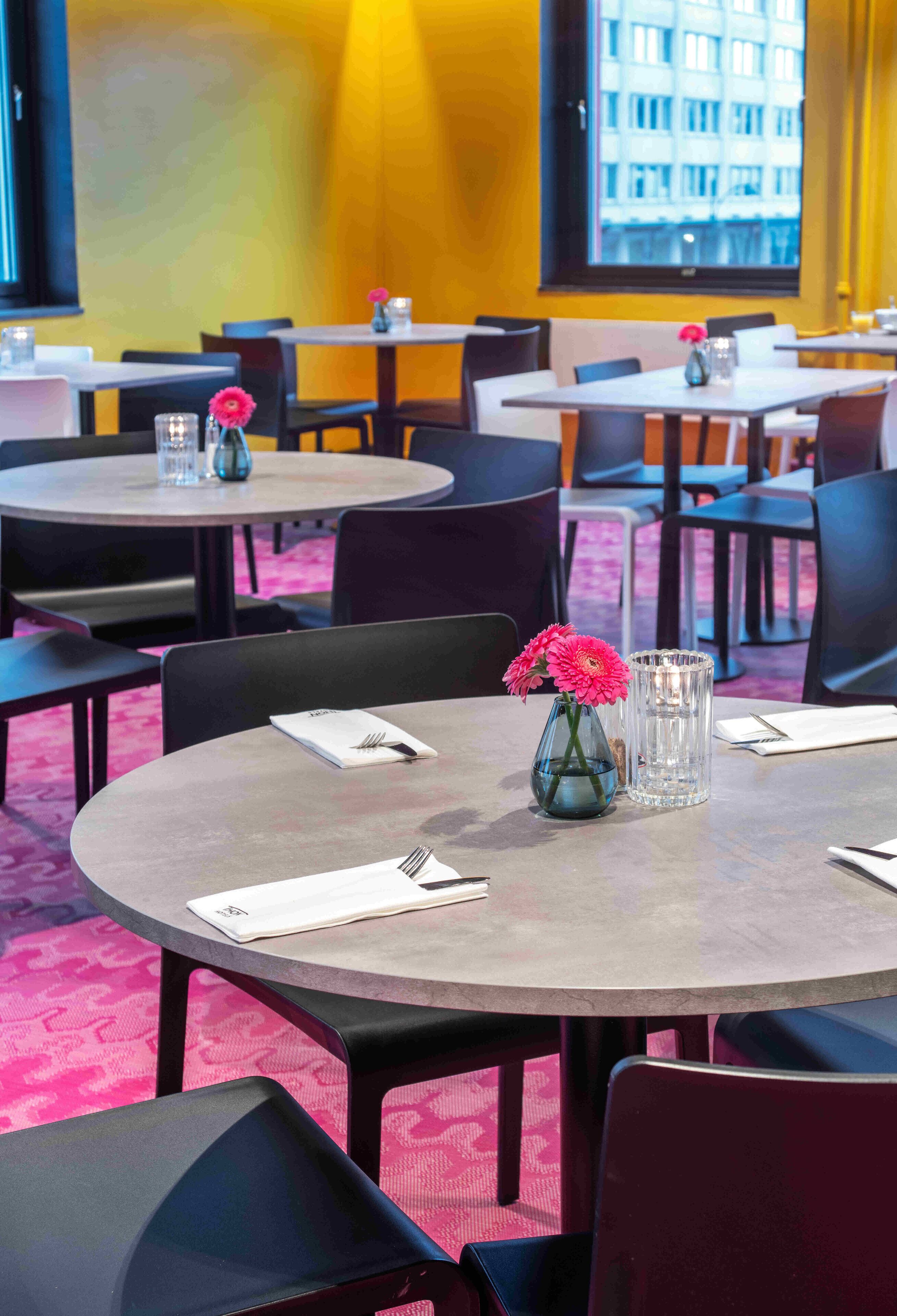 Un comedor de hotel con mesas redondas, sillas y un jarrón con flores.