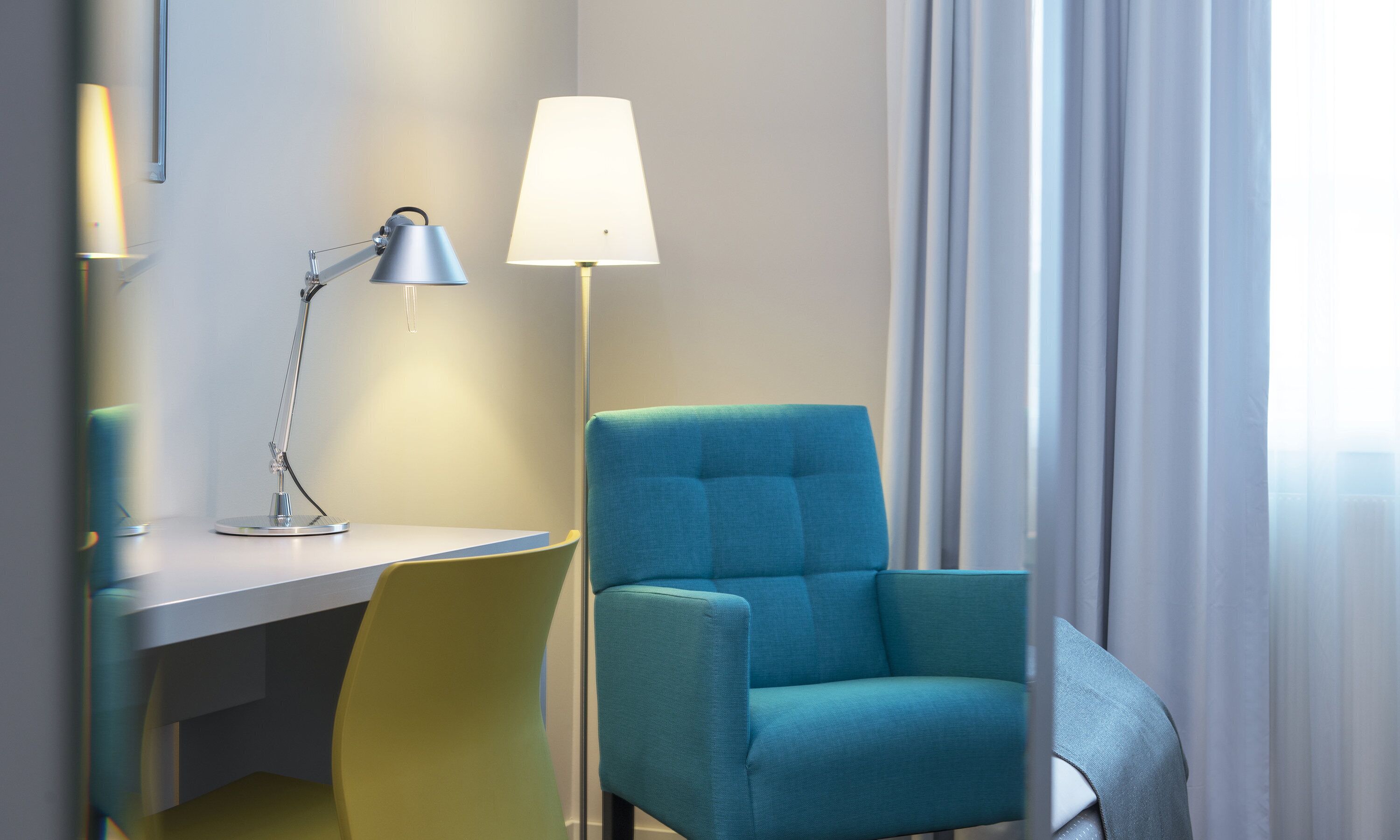 A room with a desk, a chair, a lamp, and a window with curtains.