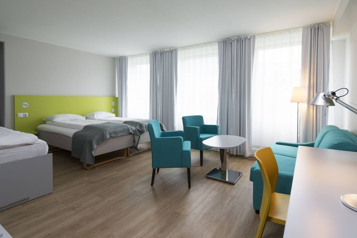 A hotel room with a bed, two chairs, a small table, and a desk.