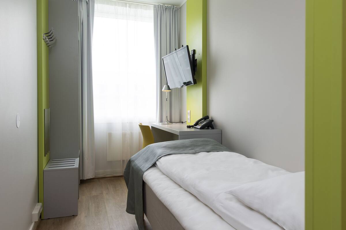 A hotel room with a bed, a desk with a chair, a telephone, and a mirror on the wall.