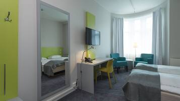 Une chambre d’hôtel avec un lit, un bureau et une chaise, une télévision et une fenêtre avec des rideaux.