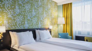 Habitación de hotel con una cama grande, dos lámparas de noche, una silla y un ventanal con cortinas.