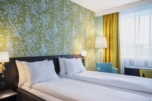 Habitación de hotel con una cama grande, dos lámparas de noche, una silla y un ventanal con cortinas.
