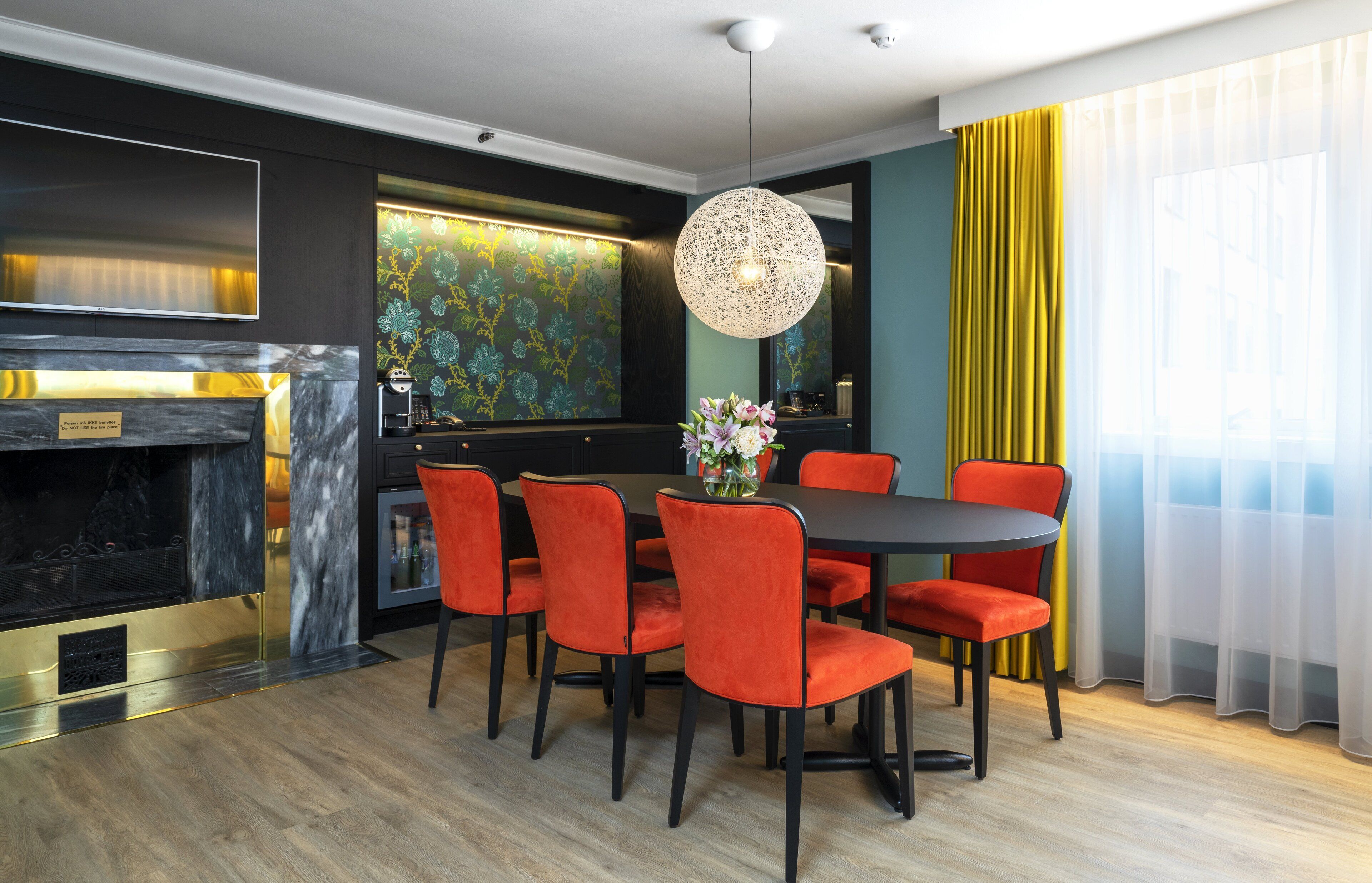 A modern dining area with a round table, six red chairs, and a decorative light fixture.