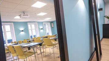 Une salle de conférence équipée de tables et de chaises, d’un projecteur et d’un luminaire fixé au mur.