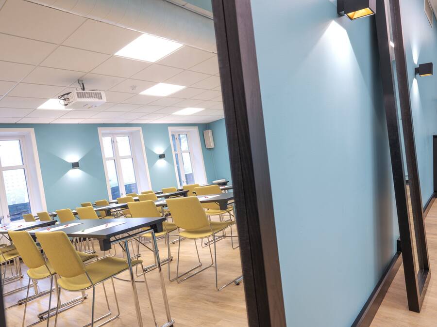 Une salle de conférence équipée de tables et de chaises, d’un projecteur et d’un luminaire fixé au mur.