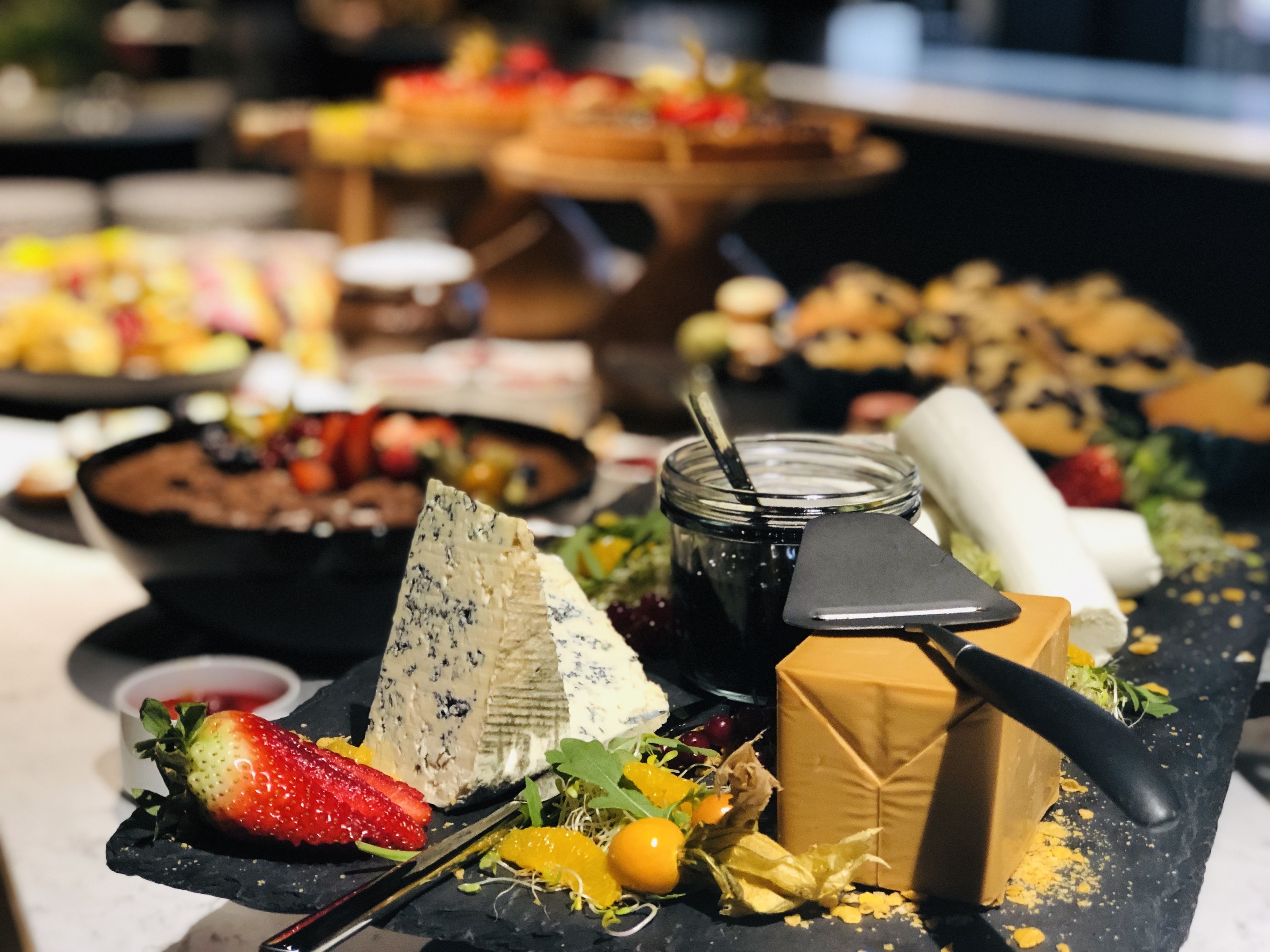 Eine Auswahl an Käse, Obst und ein Glas Marmelade auf einer Schieferplatte.