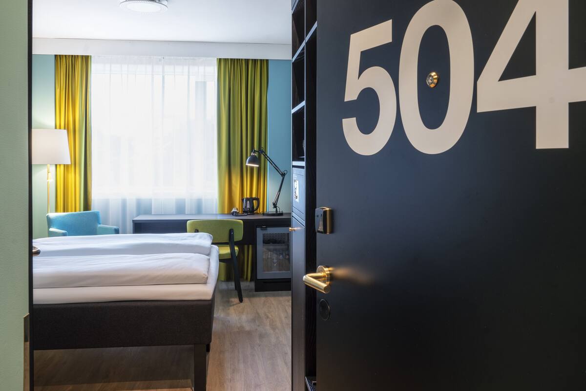 A hotel room with a bed, a desk, a chair, a lamp, and a door with the number 504.