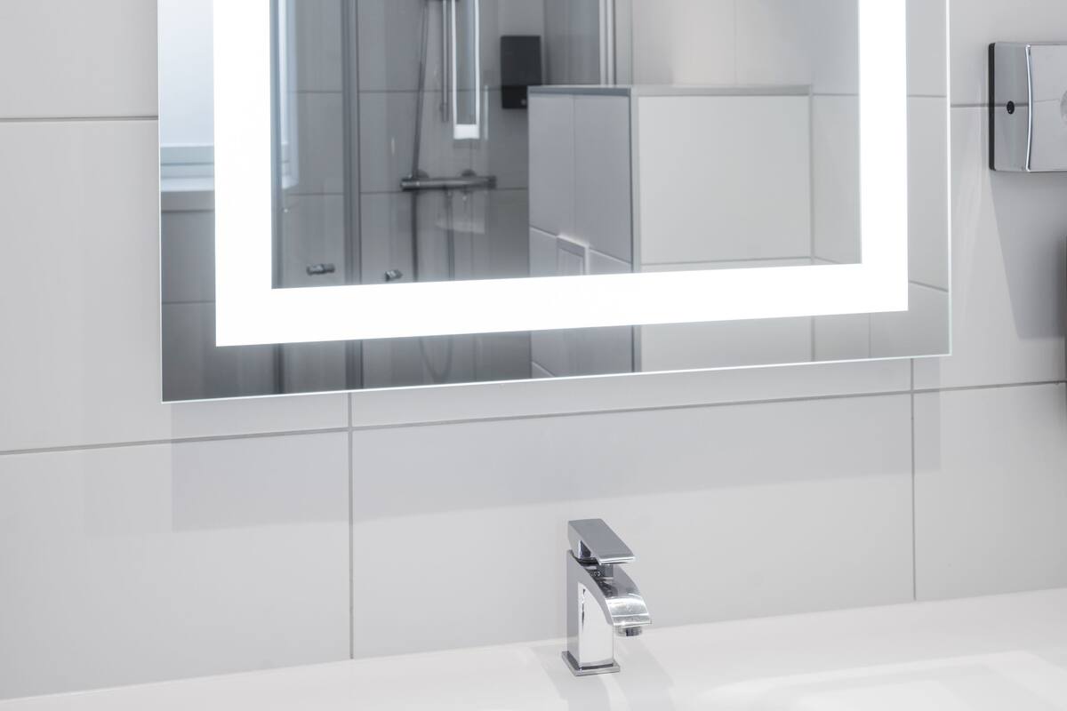 A modern bathroom with a large mirror, a chrome faucet, and a shower.
