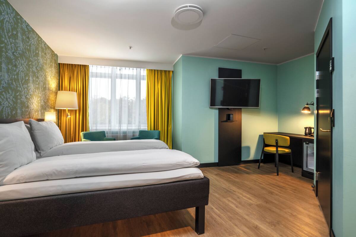 A hotel room with a bed, a desk, a chair, a television, and a refrigerator.