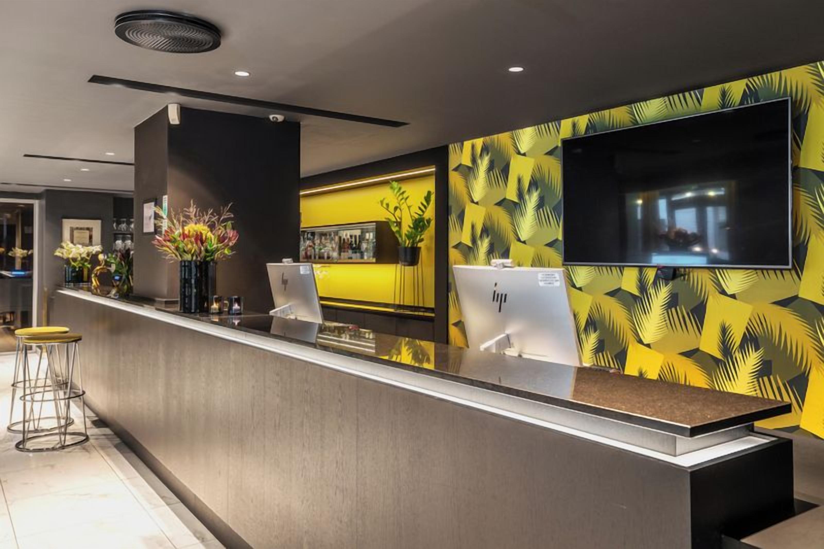 Zona de recepción con mostrador, televisor de pantalla plana en la pared y diseño moderno con una paleta de colores amarillo y negro.
