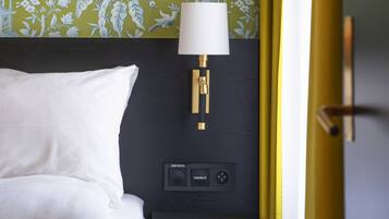 A hotel room with a bed, a nightstand with a lamp, and a wall with floral wallpaper.