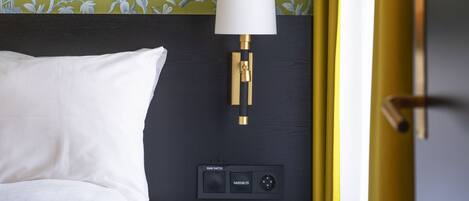 Una habitación de hotel con cama, mesita de noche con lámpara y pared con papel tapiz floral.
