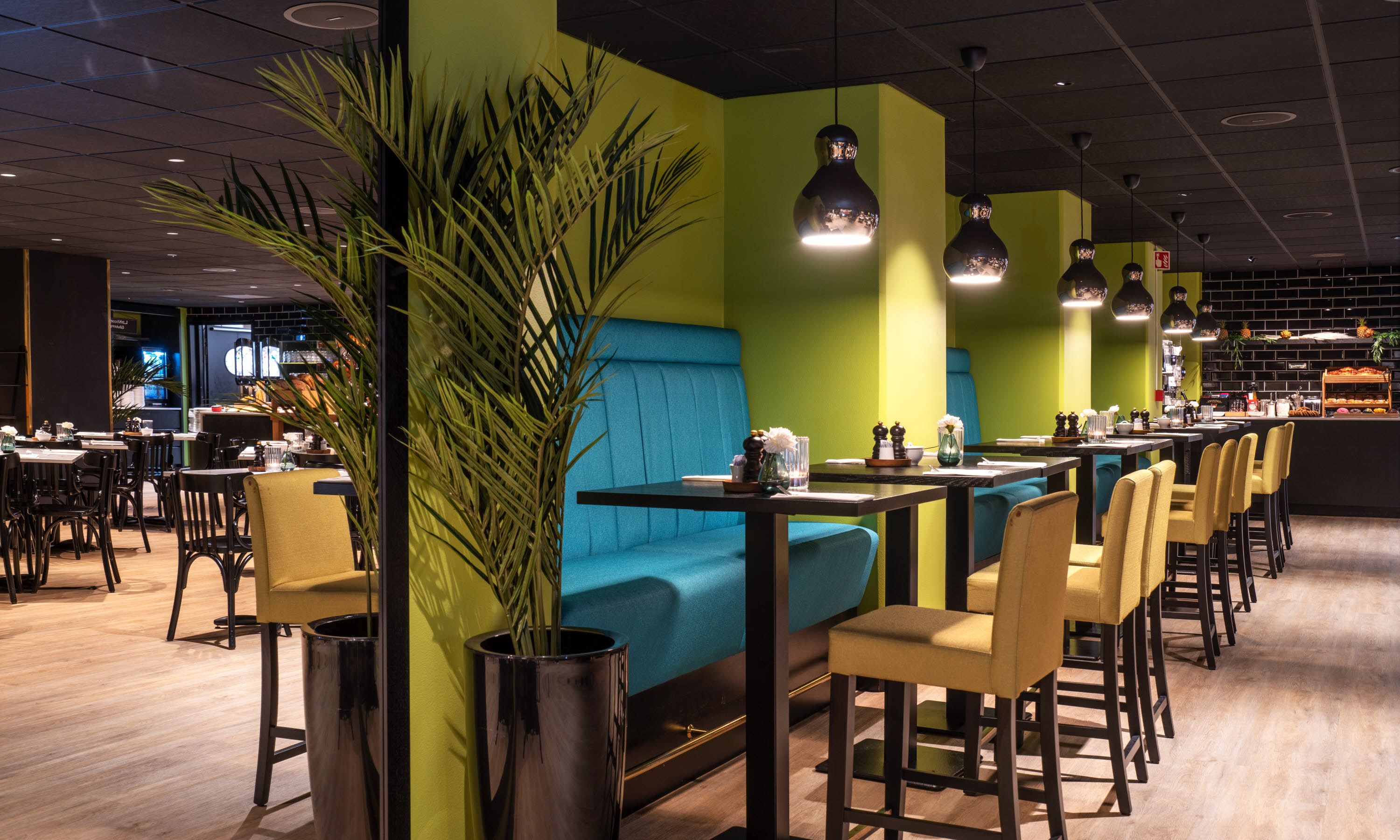 Un restaurante moderno con asientos tapizados en tono turquesa, sillas amarillas y paredes verdes.