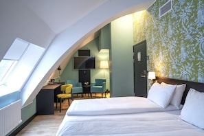 Una habitación de hotel con una cama grande, un escritorio con dos sillas, un televisor en la pared y un ventanal que proporciona luz natural.