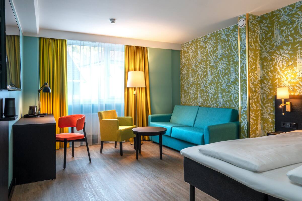A hotel room with a bed, a desk, a chair, a sofa, and a small table.