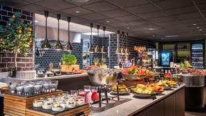 Zona de bufé con diversas opciones de comida y bebida, incluyendo frutas, verduras y refrescos.