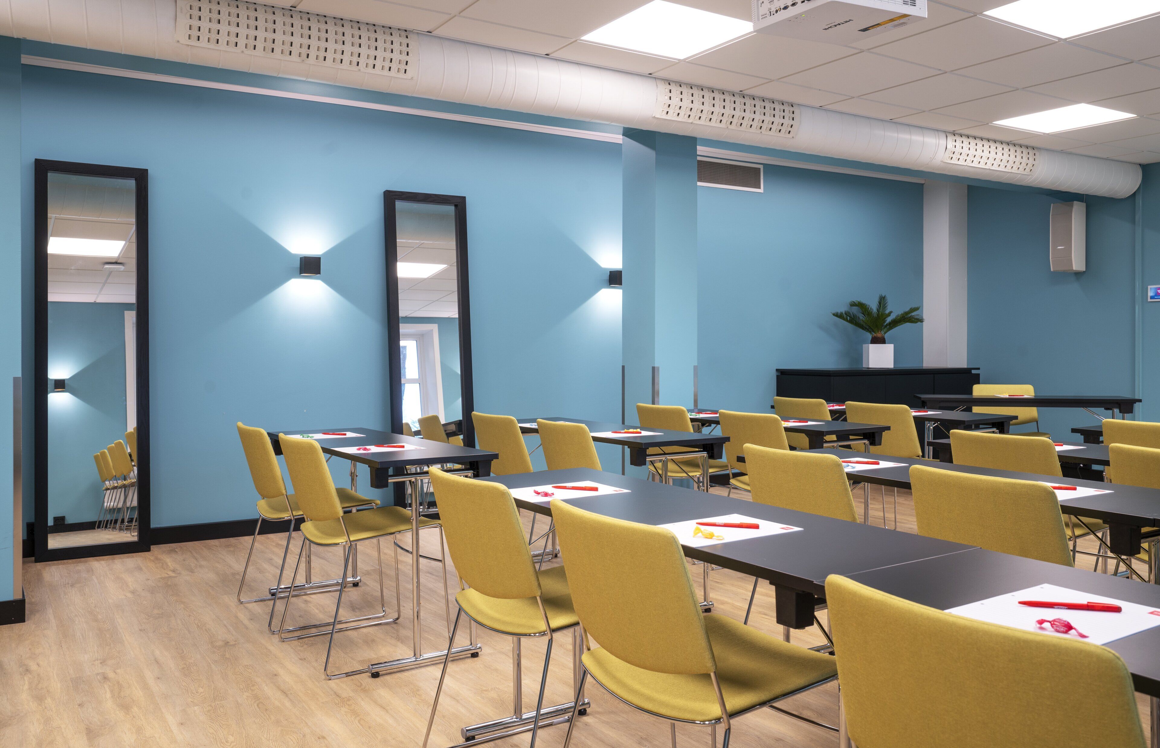 A conference room with tables and chairs, a large mirror, and a plant on a shelf.