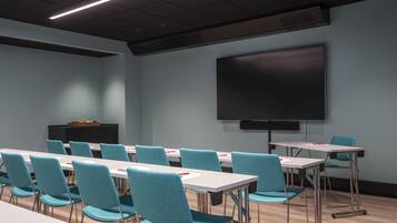 A conference room with teal chairs and white tables, a large screen, and a podium.