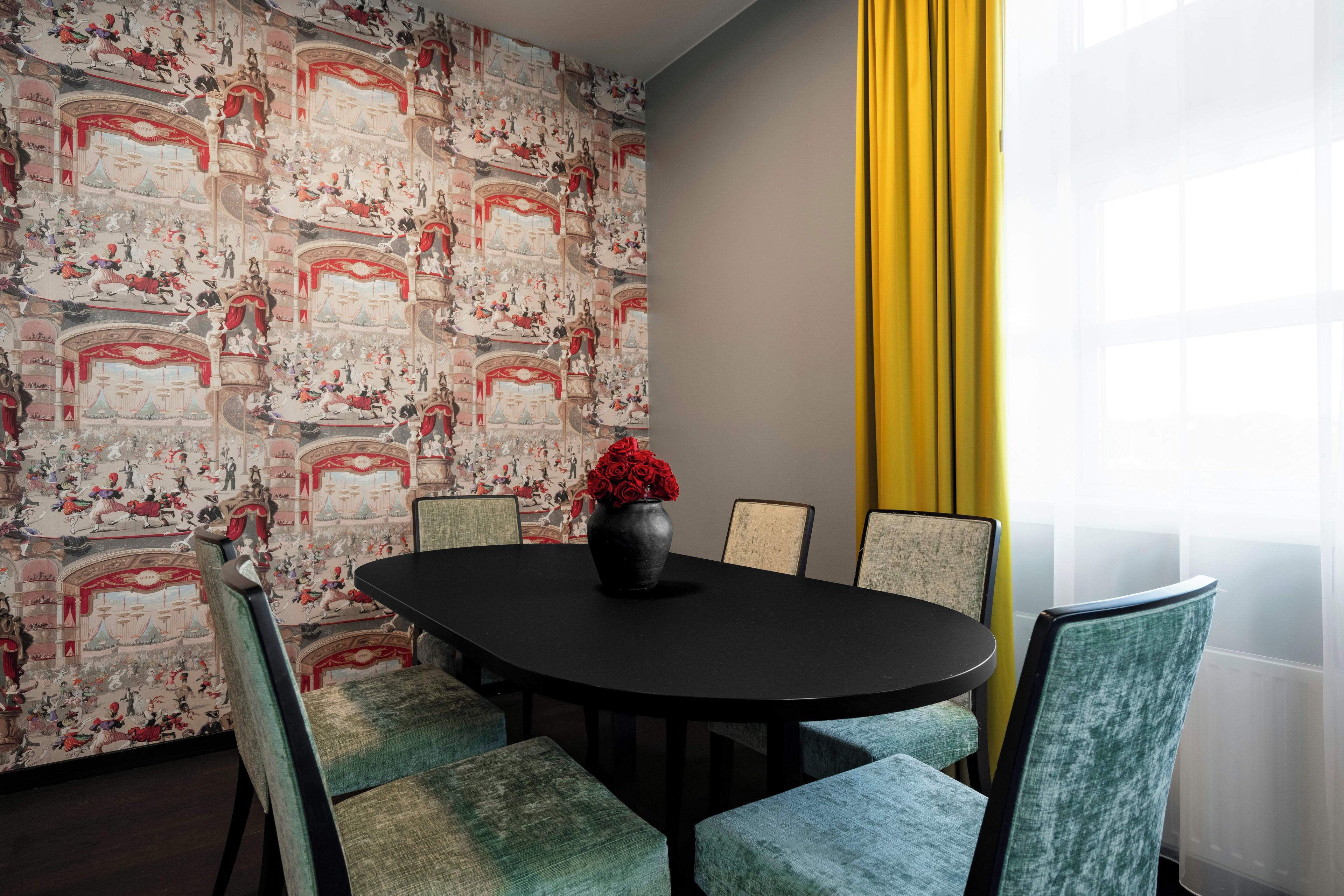 A conference room with a round table, four chairs, a vase with red flowers, and a wall with a detailed mural.