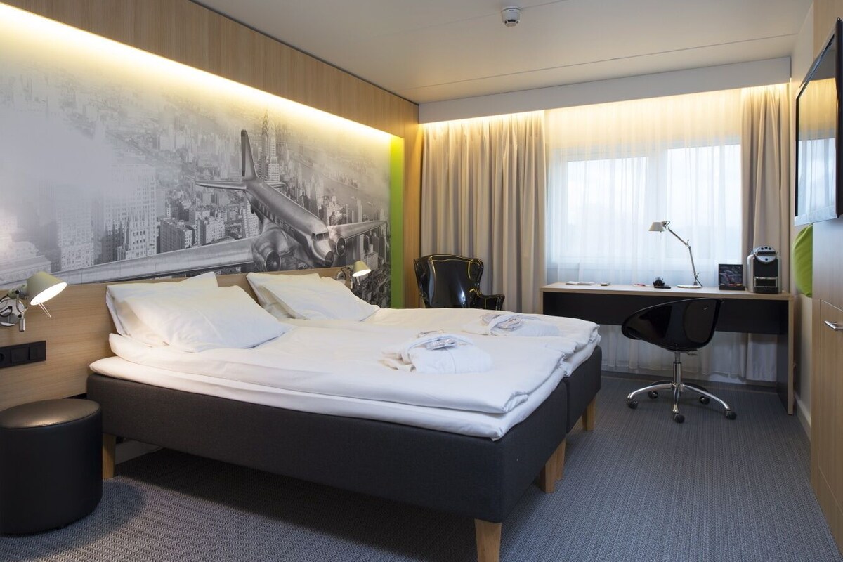 A modern hotel room with a large bed, a desk, and a chair.