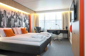 A hotel room with a large bed, a desk, a chair, and a cityscape mural on the wall.