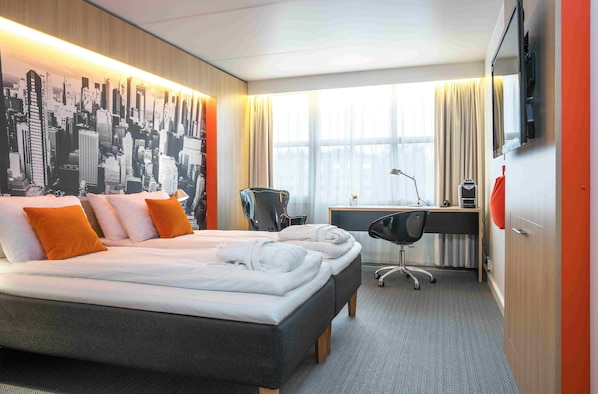 Una habitación de hotel con una cama grande, un escritorio, una silla y un mural de paisaje urbano en la pared.