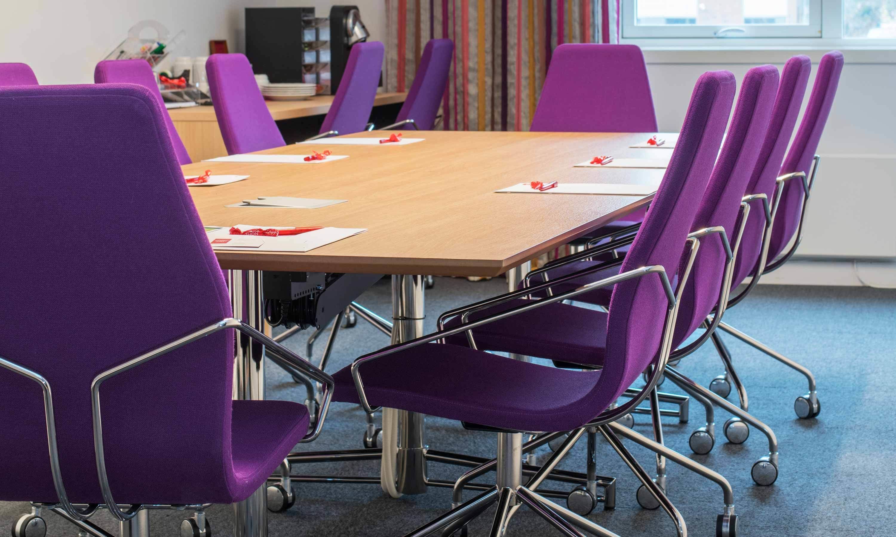 A conference room with a wooden table and purple chairs.