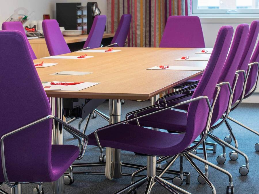 A conference room with a wooden table and purple chairs.