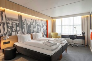 Habitación de hotel con una cama grande, un escritorio, una silla y un mural de paisaje urbano en la pared.