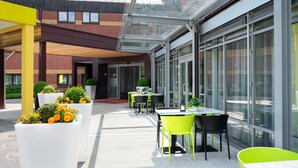 An outdoor dining area with tables and chairs, a glass enclosure, and a brick building in the background. - Thon Hotel Bergen Airport (Bergen)