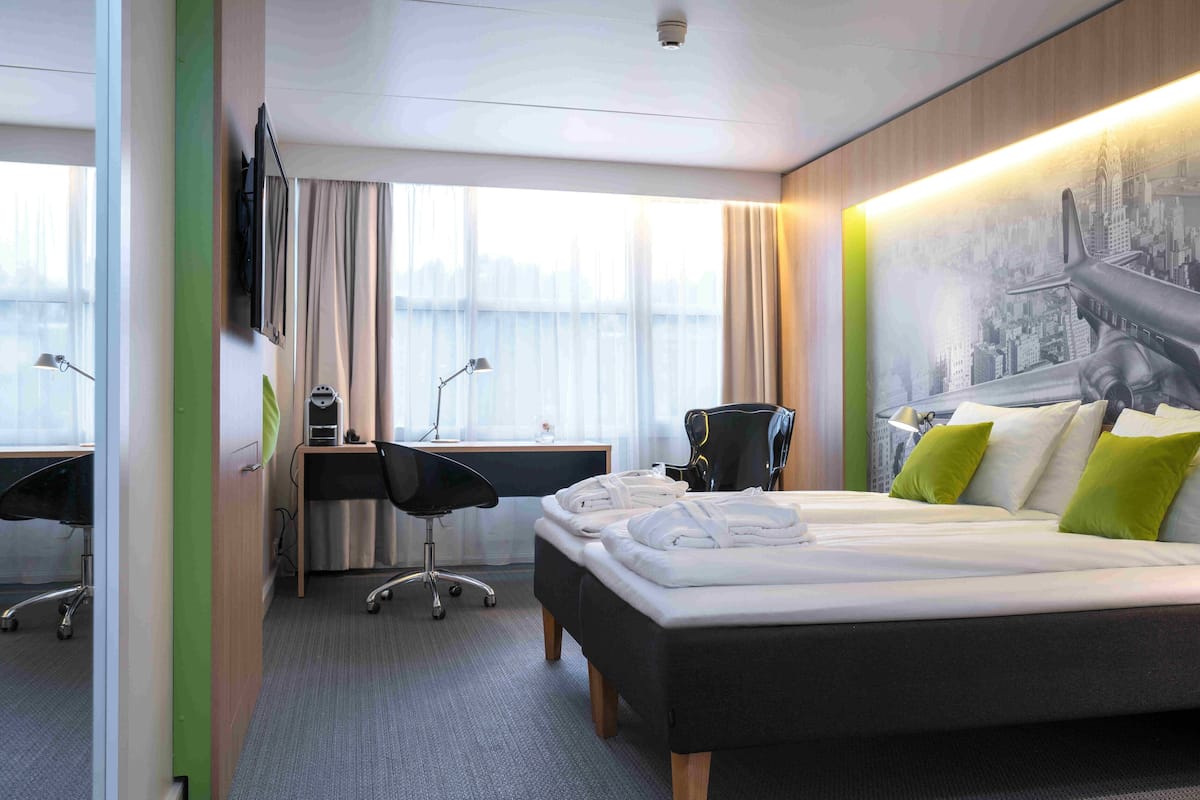 A hotel room with a bed, desk, chair, and a large window.