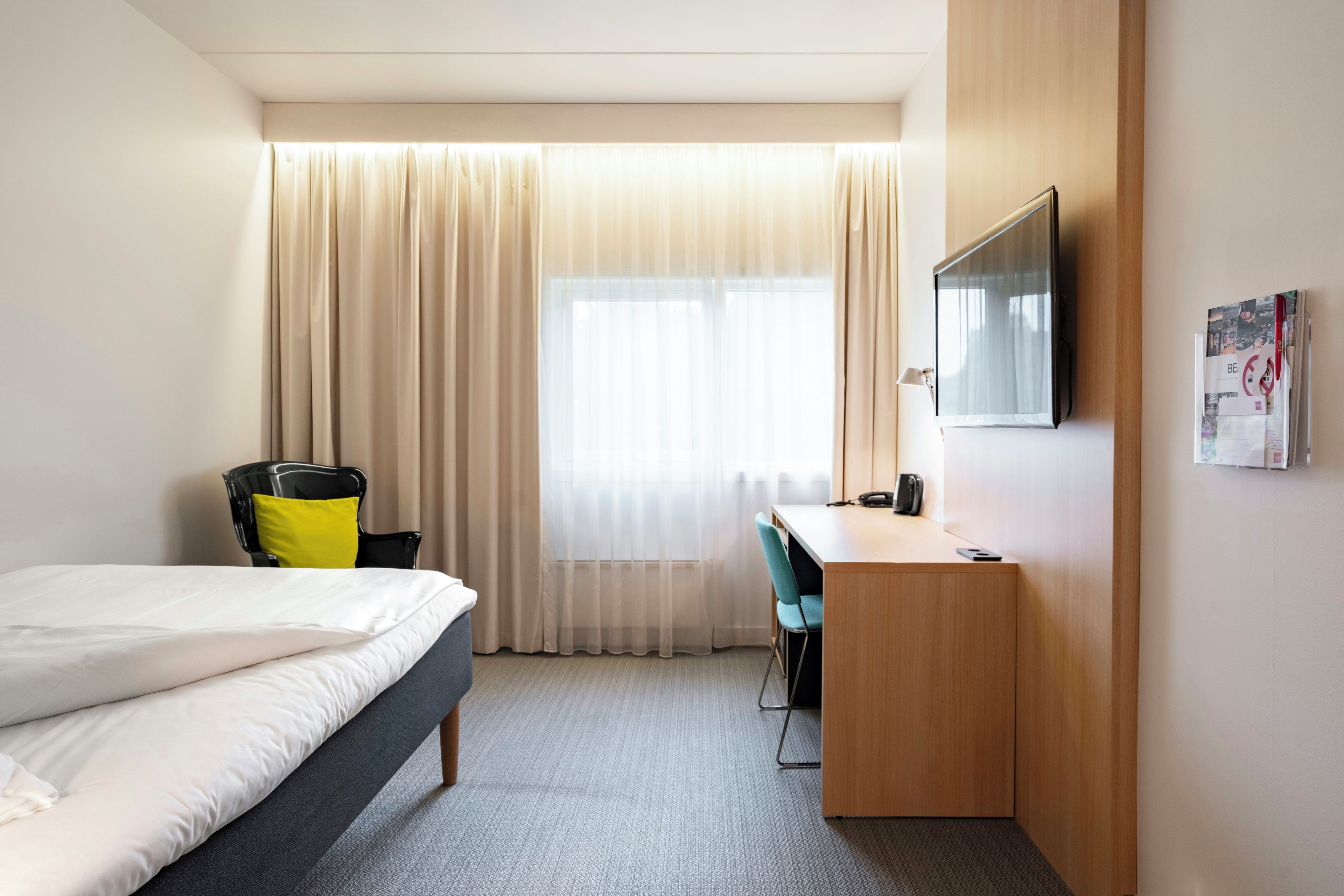 A hotel room with a bed, a desk, a chair, a television, and a window with curtains.