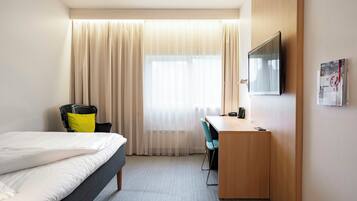A hotel room with a bed, a desk, a chair, a television, and a window with curtains.