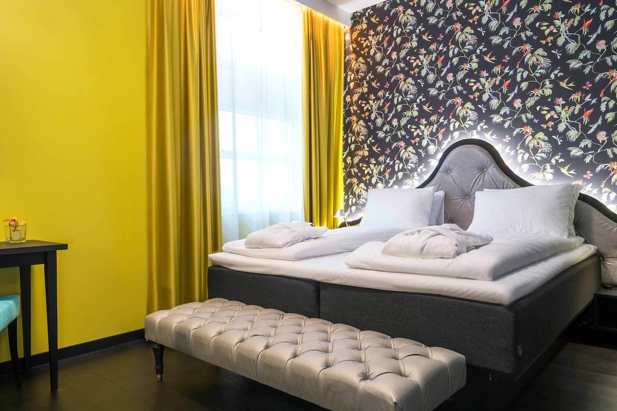 A hotel room with a bed, a bench, a small table, and a chair.