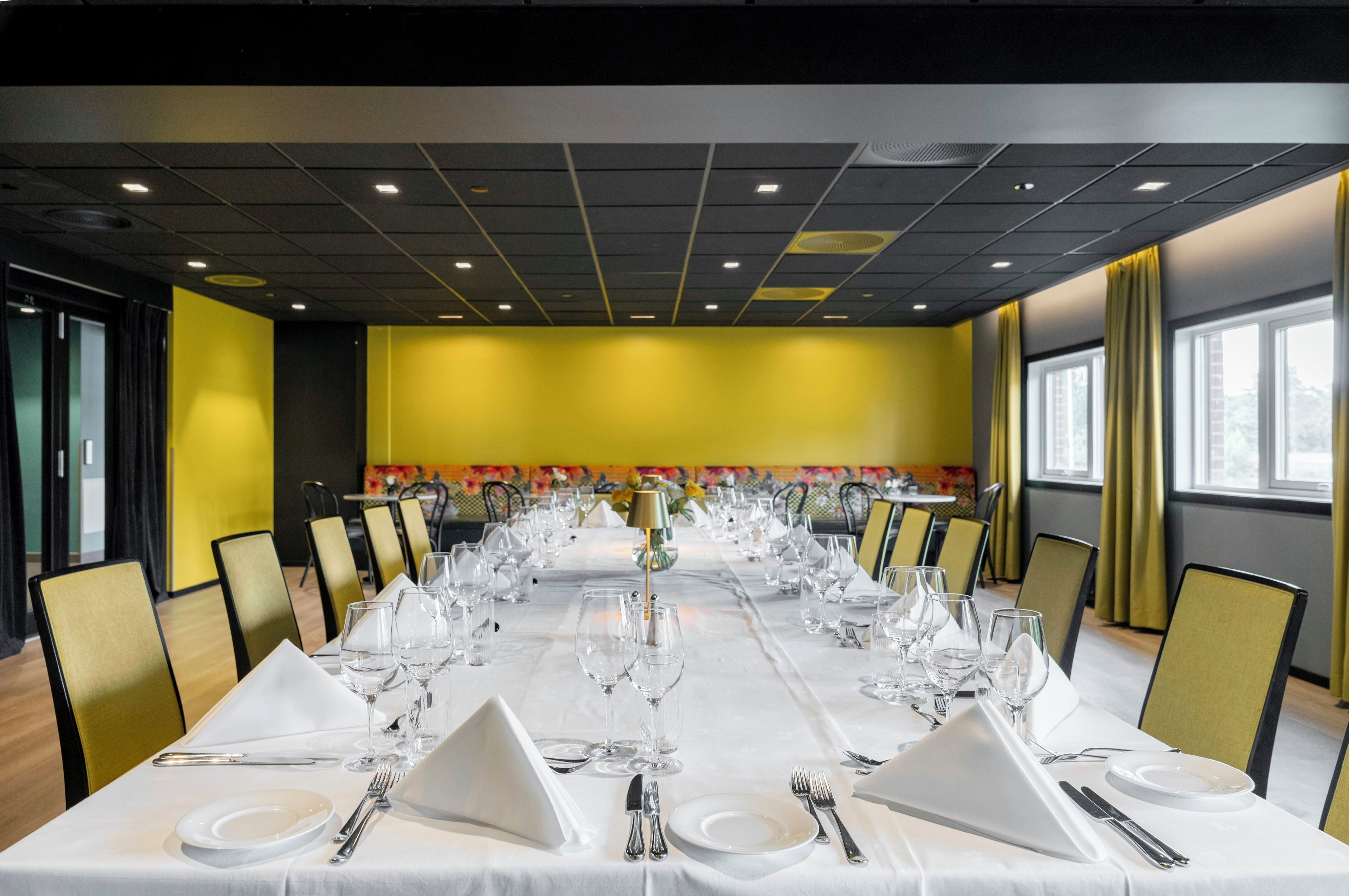 A conference room with a long table set for a formal event, equipped with chairs, tables, and glassware.