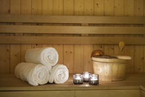 A wooden sauna with rolled white towels, candles, and a wooden bucket with a wooden mallet.