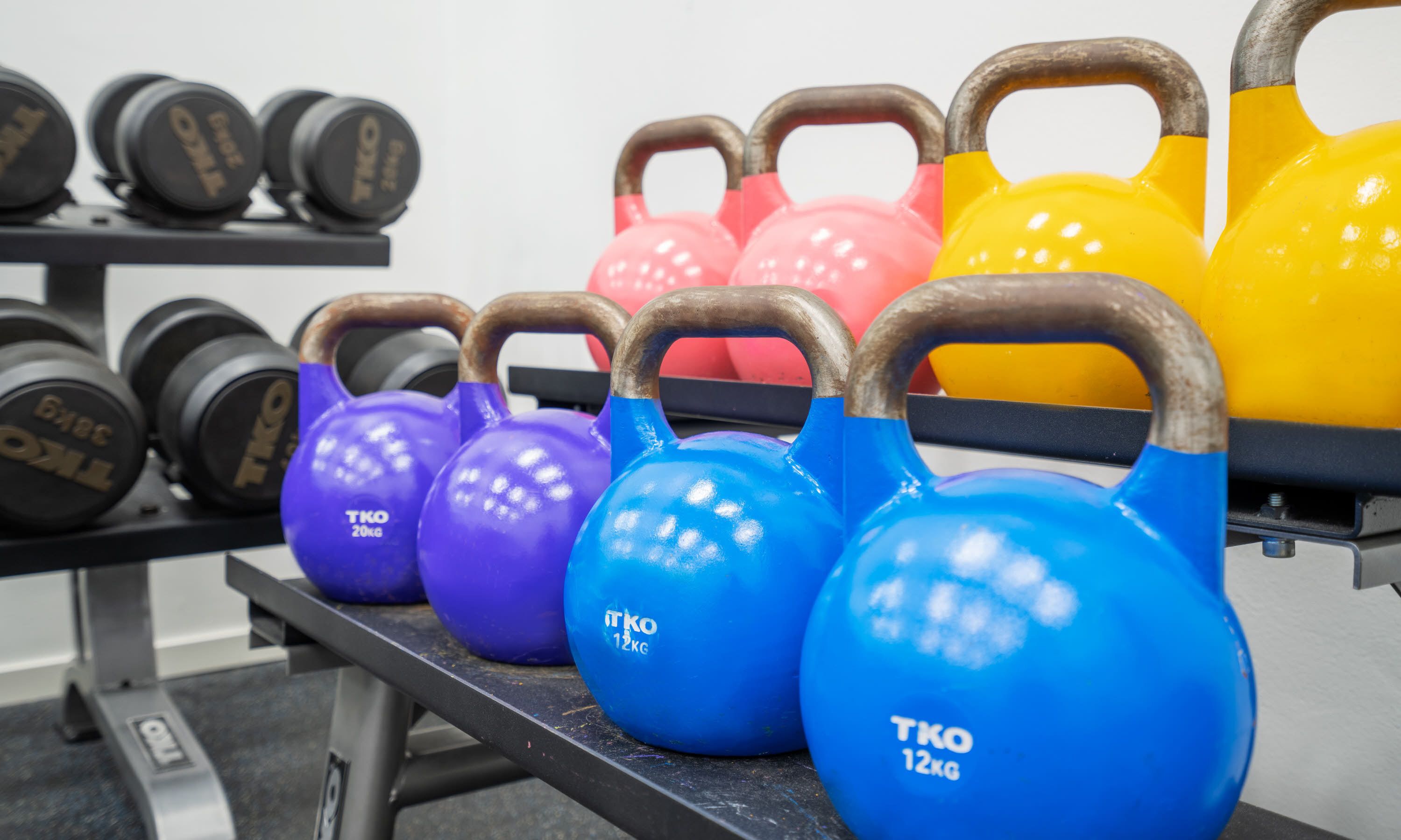 Kettlebells in verschillende kleuren en gewichten, netjes op een rek geplaatst.