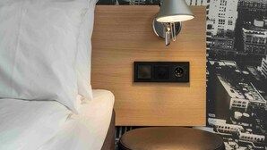 A hotel room with a bed, a wooden nightstand with a lamp, and a wall mural of a cityscape. - Thon Hotel Bergen Airport (Bergen)