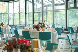 Comedor con mesas dispuestas para una comida, sillas y ventanas amplias con vistas a zonas verdes.