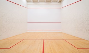 A squash court with wooden flooring and red boundary lines.