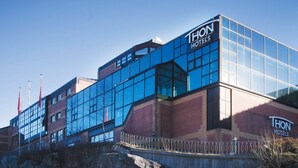 A THON Hotels building with a modern glass facade, a brick base, and a metal fence in front. - Thon Hotel Bergen Airport (Bergen)