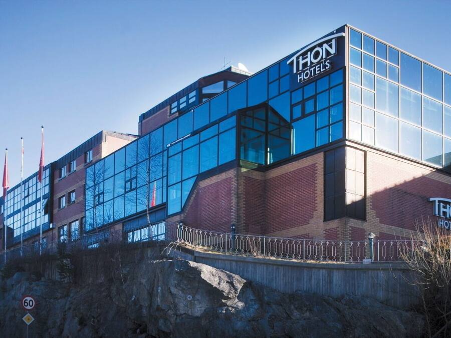 Un edificio de THON Hotels con fachada de vidrio moderna, base de ladrillo y una valla metálica al frente.