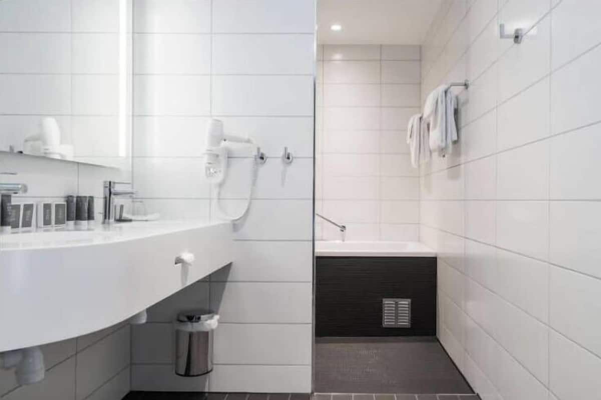 A modern bathroom with white tiles, a shower, a sink, and a trash can.
